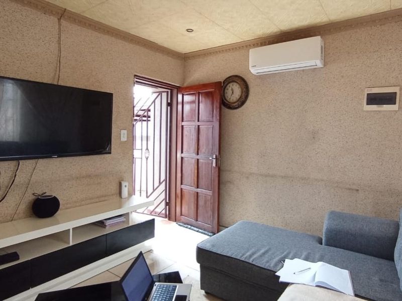 A living room featuring tiled flooring, a wall-mounted air conditioning unit, and textured wall finishes with direct access to an exterior area.