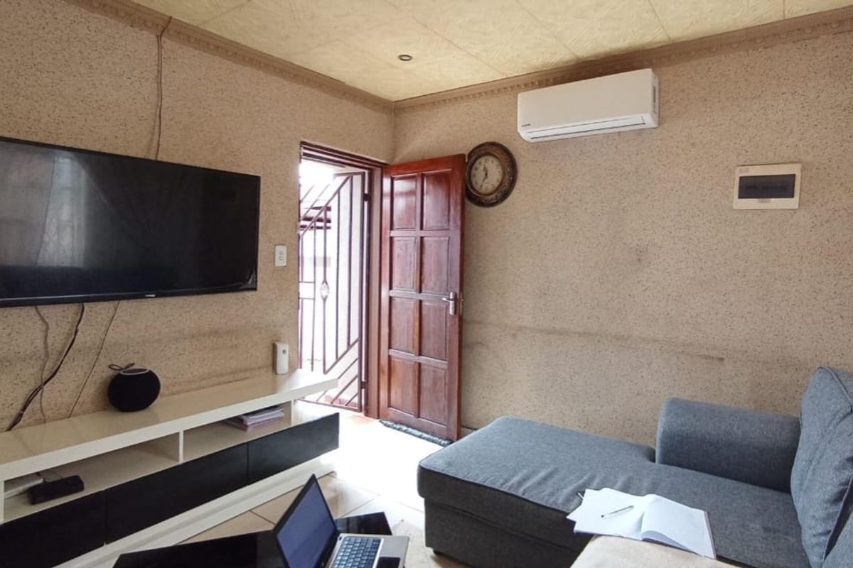 A living room featuring tiled flooring, a wall-mounted air conditioning unit, and textured wall finishes with direct access to an exterior area.