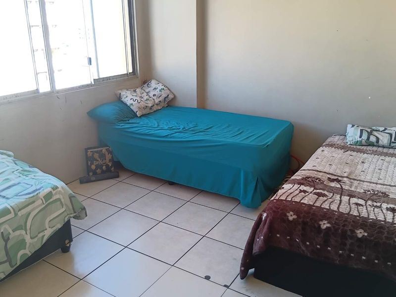 A bedroom featuring tiled flooring and a large sliding window, currently configured with multiple beds.
