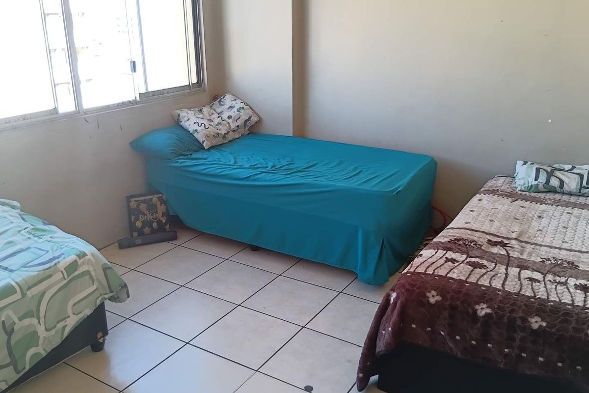 A bedroom featuring tiled flooring and a large sliding window, currently configured with multiple beds.