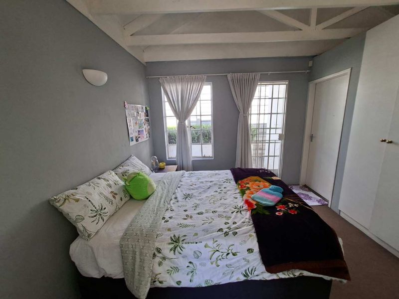 A cozy bedroom featuring exposed ceiling beams, built-in wardrobe storage, and direct access to the exterior via a security-gated door.