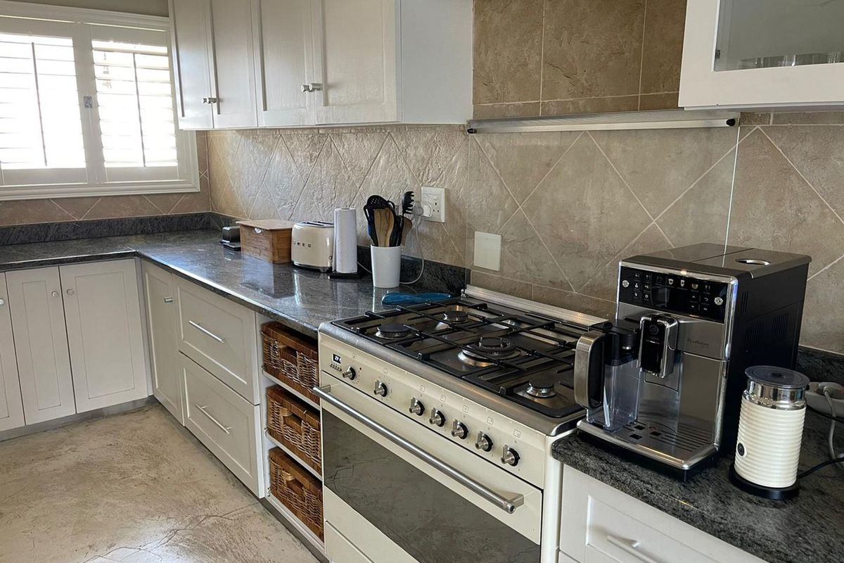 A functional kitchen featuring white cabinetry, granite countertops, a gas stove with extractor fan, and tiled backsplash.