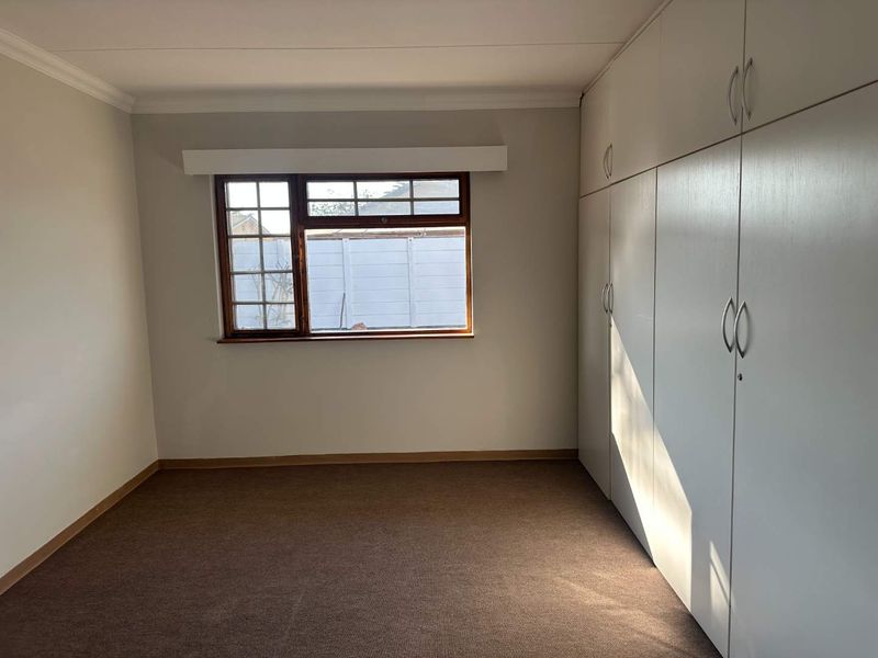 A clean, empty bedroom featuring neutral walls, carpeted flooring, and extensive built-in cupboard storage with a window overlooking the rear exterior.