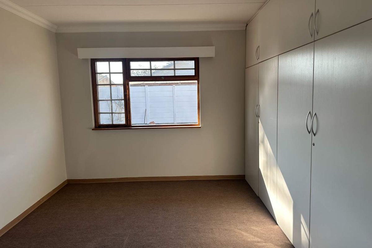 A clean, empty bedroom featuring neutral walls, carpeted flooring, and extensive built-in cupboard storage with a window overlooking the rear exterior.