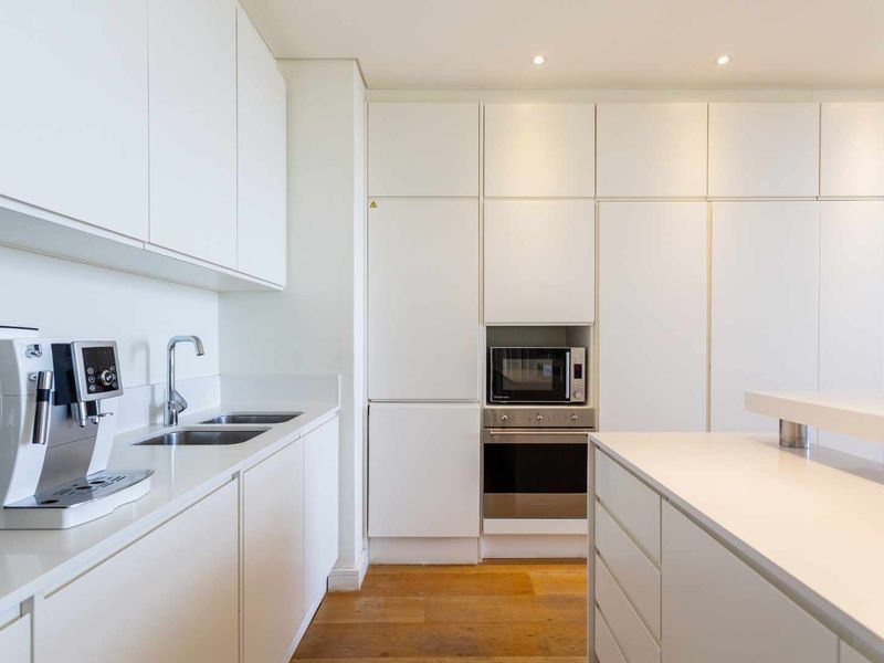 Modern kitchen featuring sleek white cabinetry, integrated appliances including an oven and microwave, stone countertops, and warm hardwood flooring.