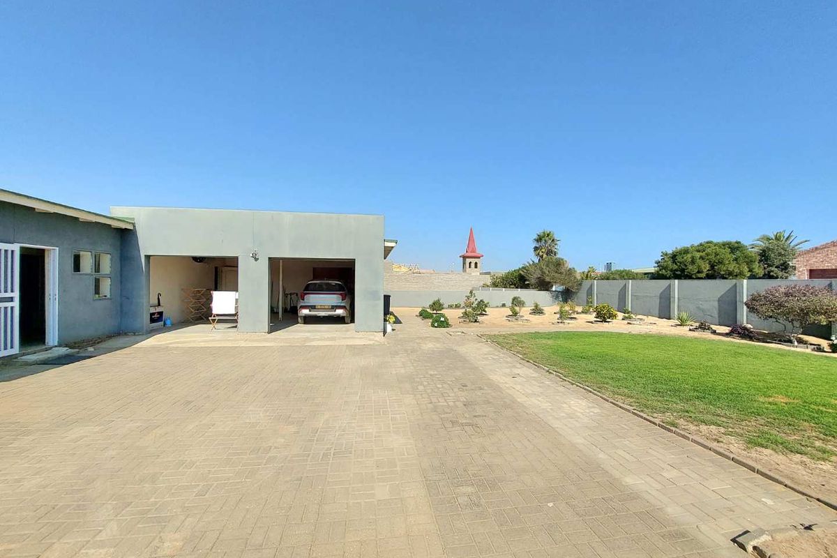 Spacious rear exterior featuring a large paved driveway, double garage, well-maintained lawn, and perimeter boundary wall.