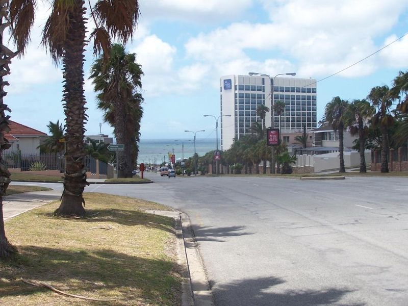 A street view showing the surrounding neighbourhood approach, featuring palm-lined roads and a view towards the coast and nearby high-rise buildings.