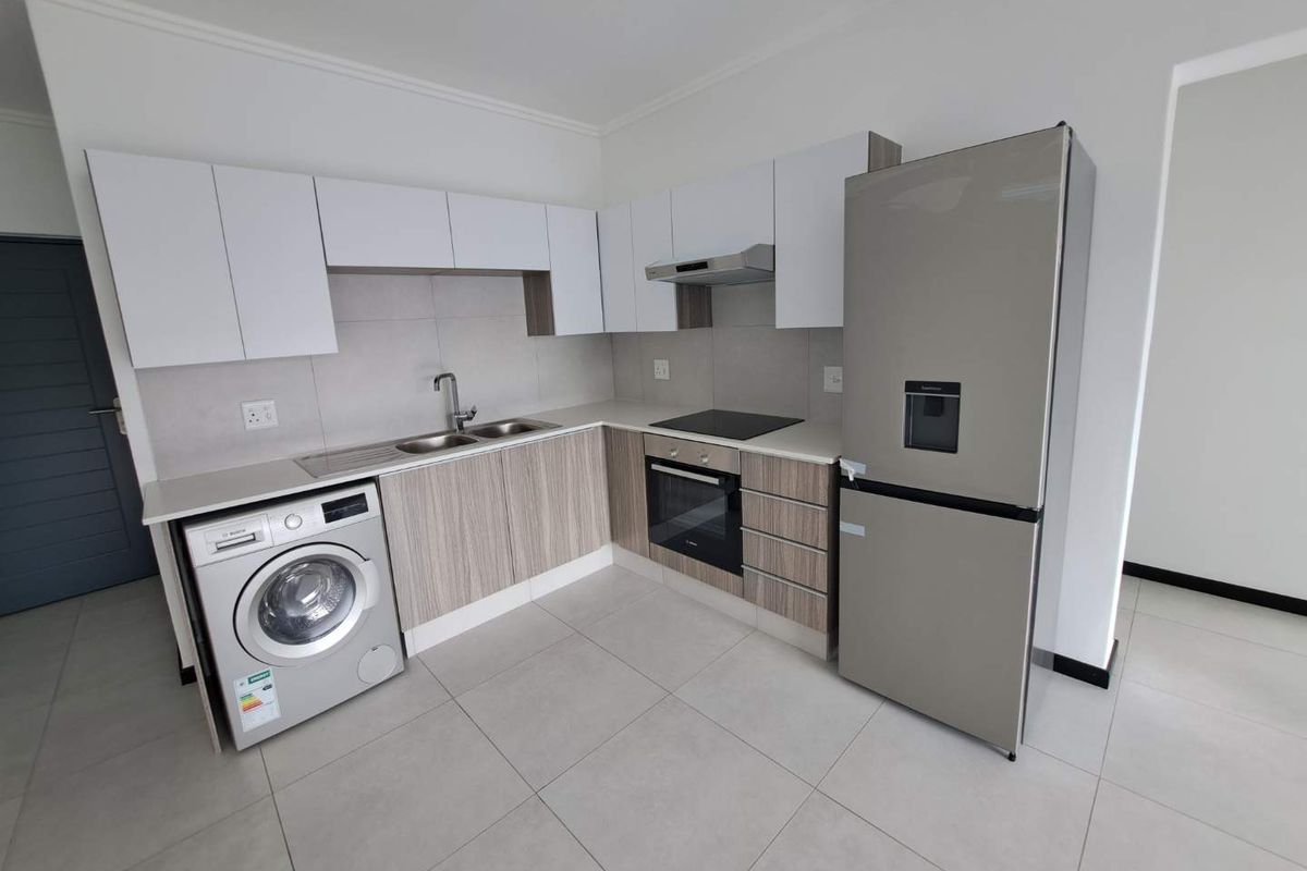 Modern kitchen featuring sleek cabinetry, stone countertops, integrated oven, hob, extractor fan, and tiled flooring in a clean, contemporary layout.