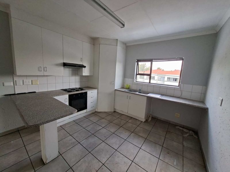 A functional, empty kitchen featuring white built-in cabinetry, laminate countertops, a built-in oven with hob, and tiled flooring throughout.