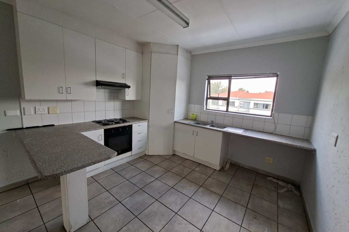 A functional, empty kitchen featuring white built-in cabinetry, laminate countertops, a built-in oven with hob, and tiled flooring throughout.