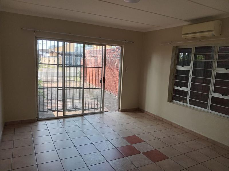 An empty living room featuring tiled flooring, a sliding glass door with security gate, and a wall-mounted air conditioning unit.