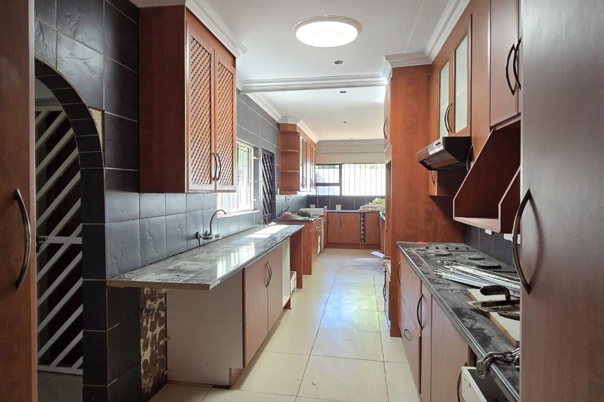A galley-style kitchen featuring wooden cabinetry, dark tiled splashbacks, and stone-look countertops, currently undergoing minor maintenance or renovation.