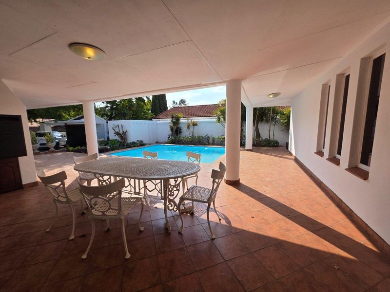 Spacious covered patio area featuring tiled flooring and structural columns, overlooking a private swimming pool and garden.
