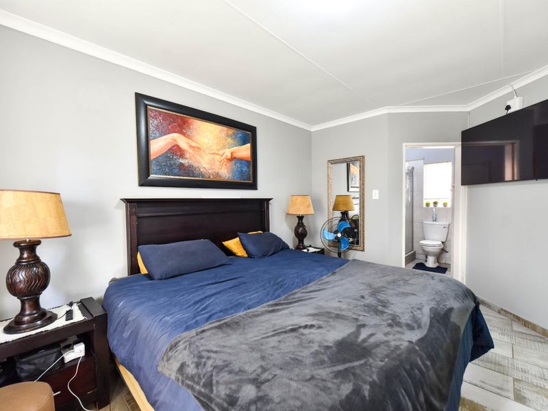 A well-maintained bedroom featuring tiled flooring, coved ceilings, and an attached en-suite bathroom.