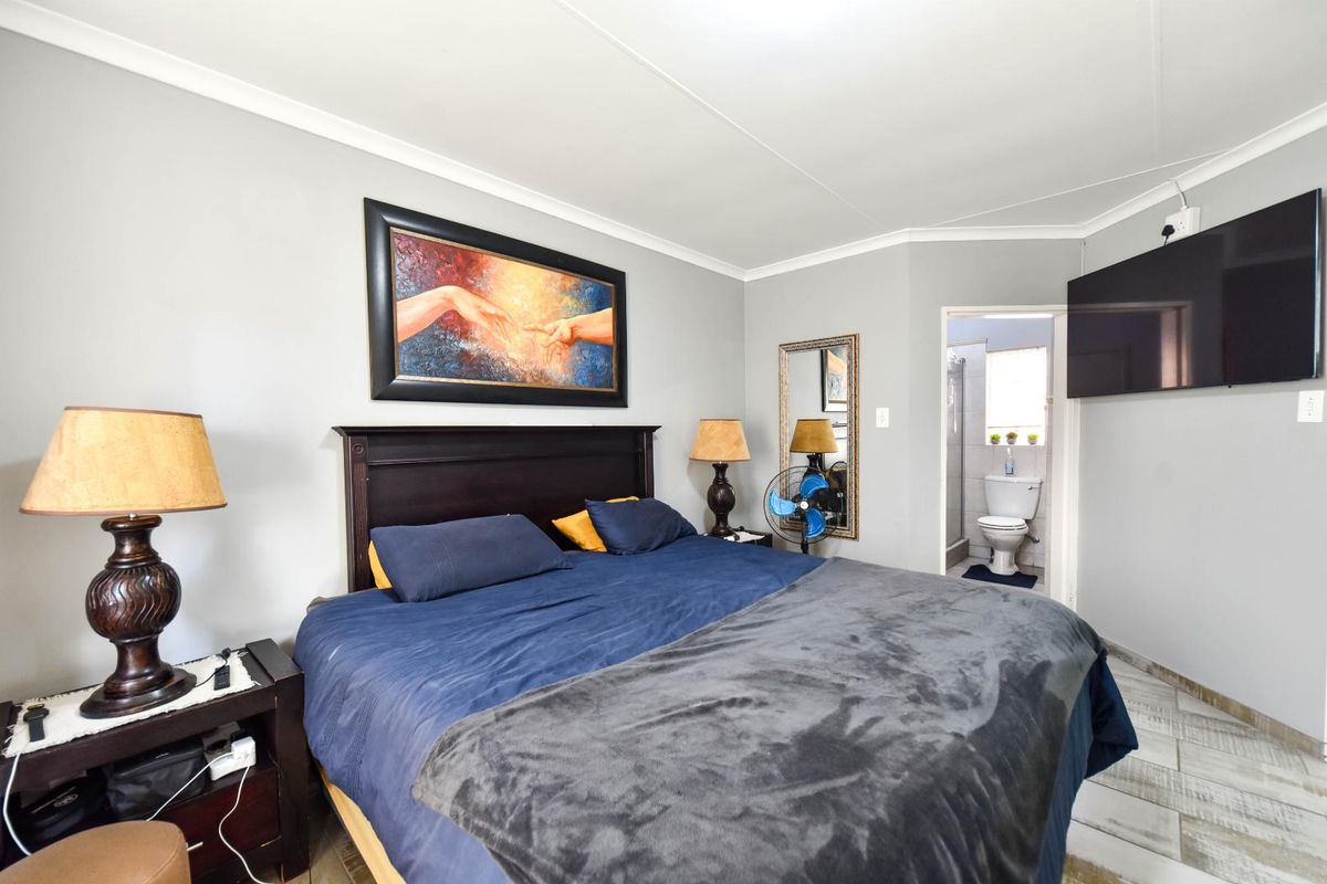 A well-maintained bedroom featuring tiled flooring, coved ceilings, and an attached en-suite bathroom.