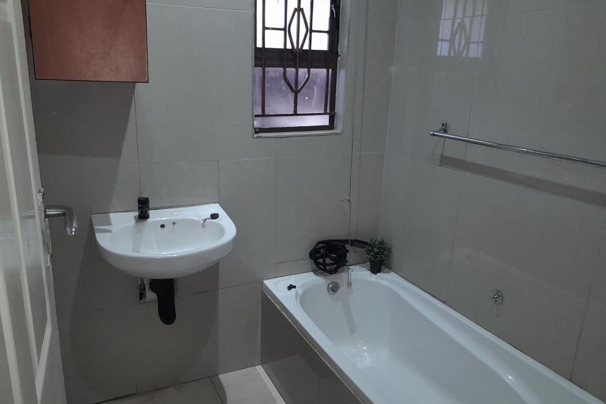 A functional bathroom featuring a wall-mounted basin, a built-in bathtub, and tiled walls with a security-grille window.