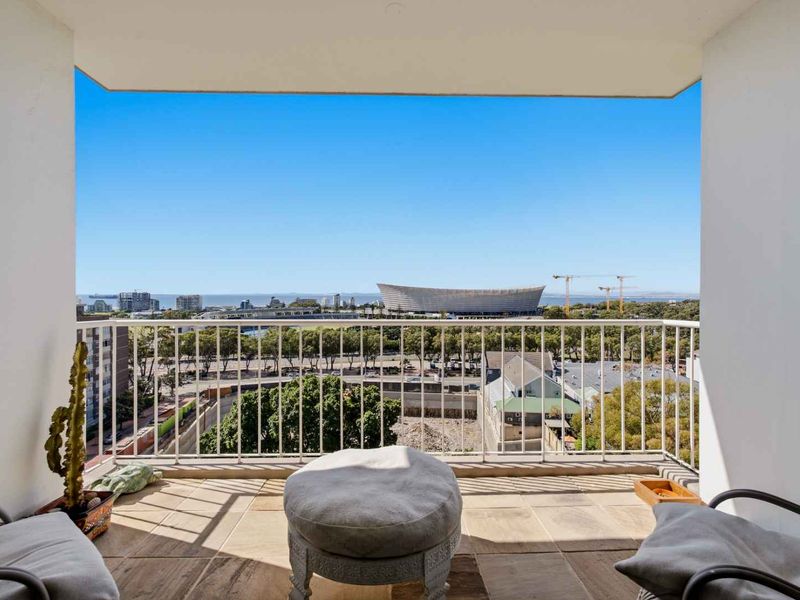 A covered balcony featuring tiled flooring and a metal balustrade, offering expansive elevated views of the surrounding cityscape and stadium.
