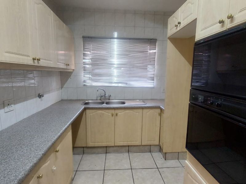 A functional kitchen featuring laminate cabinetry, granite-look countertops, a double bowl sink, and a built-in double oven with tiled finishes throughout.