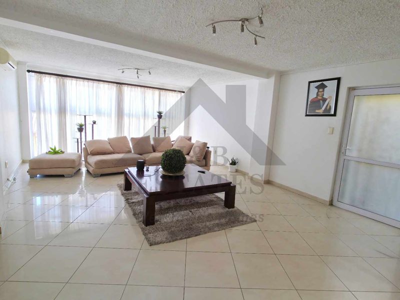 Spacious living room featuring neutral tiled flooring, a popcorn ceiling, and a split-system air conditioner, with large windows providing ample natural light.