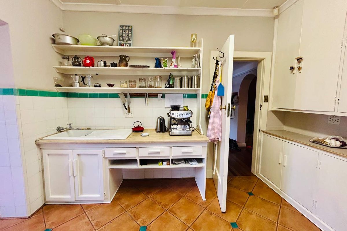 A functional kitchen area featuring built-in cabinetry, open shelving, a ceramic sink, and terracotta floor tiles with decorative accents.