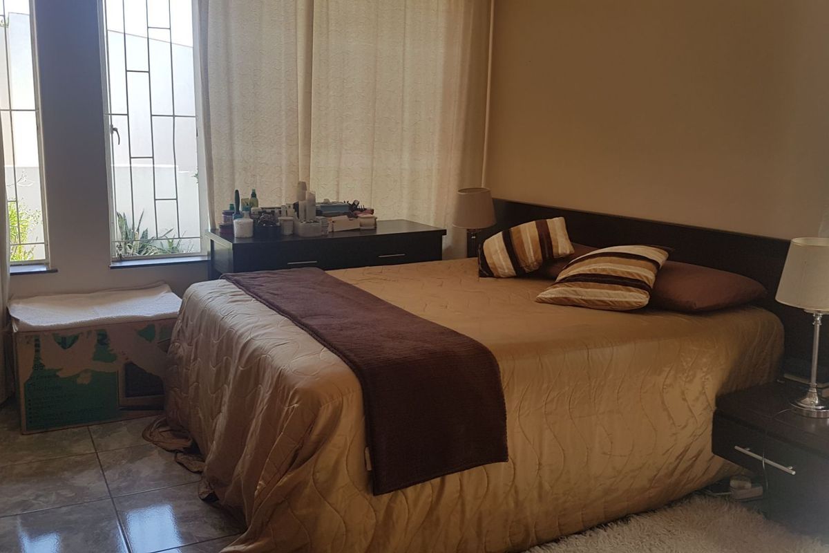 A bedroom featuring tiled flooring and a window with security bars, providing natural light and a functional layout.