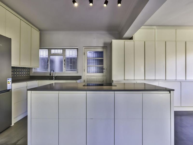 Modern kitchen featuring a central island, extensive built-in cabinetry, integrated cooktop, and sleek finishes, providing a clean and functional culinary space.
