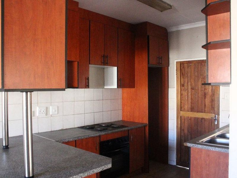 A functional kitchen featuring wood-finish cabinetry, laminate countertops, a built-in oven and hob, and a tiled backsplash.