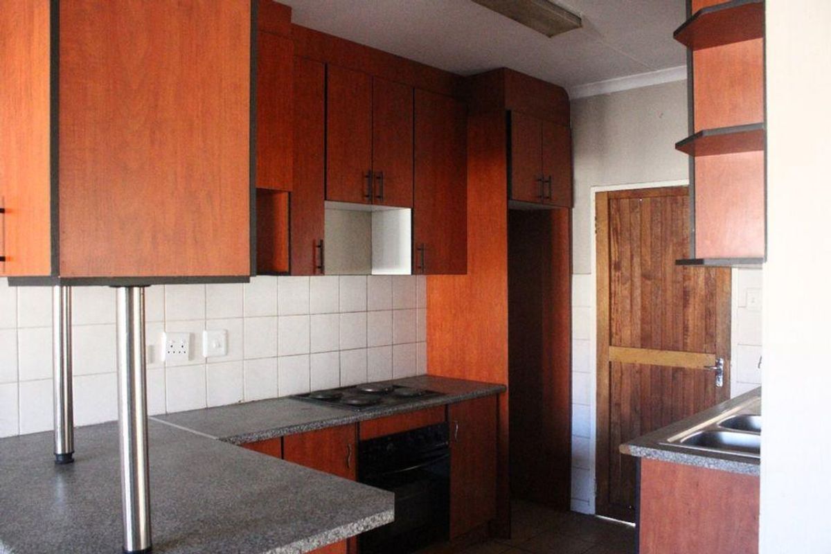 A functional kitchen featuring wood-finish cabinetry, laminate countertops, a built-in oven and hob, and a tiled backsplash.