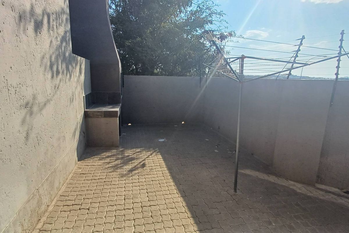 A private rear courtyard featuring paved flooring, a built-in braai area, and perimeter walling with security fencing.