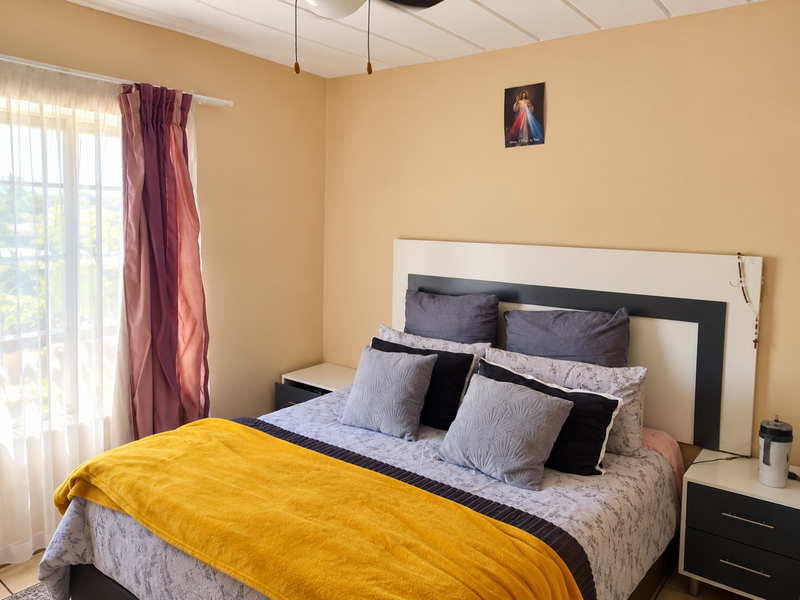 A comfortable bedroom featuring a built-in headboard, ceiling fan, and natural light from the window.