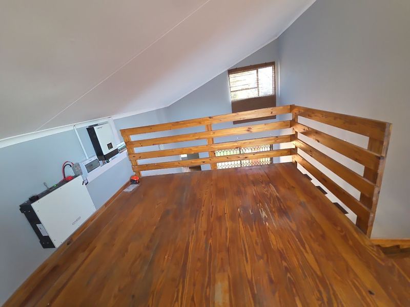 A mezzanine level bedroom featuring timber flooring, a wooden balustrade, and an integrated solar power system with inverter and battery storage.