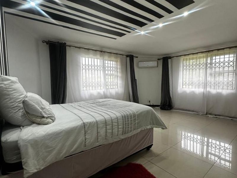 Spacious bedroom featuring large format floor tiles, a decorative striped ceiling design, and security bars on the windows.