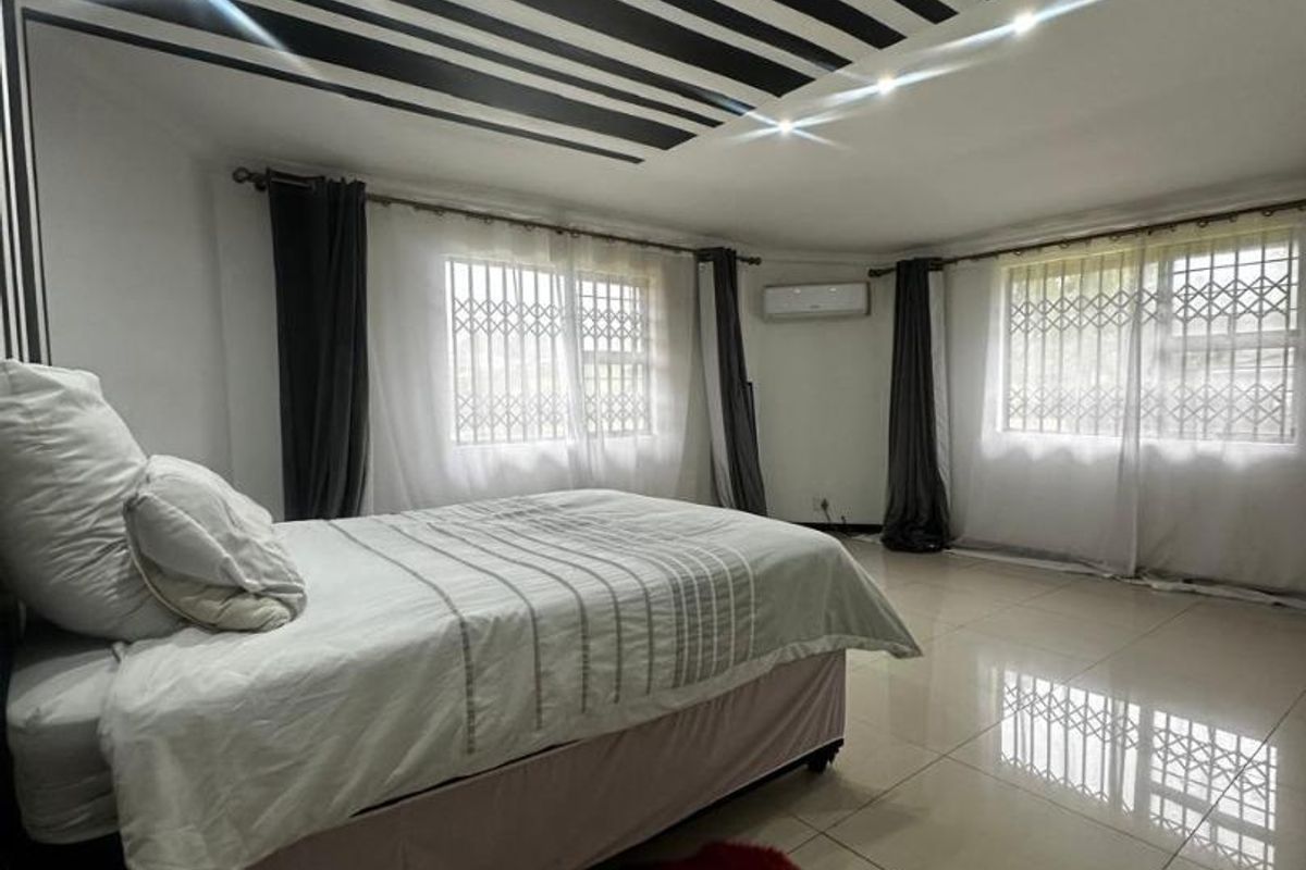 Spacious bedroom featuring large format floor tiles, a decorative striped ceiling design, and security bars on the windows.