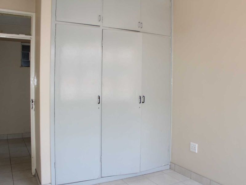 A simple bedroom featuring built-in cupboards with overhead storage and tiled flooring, offering a blank canvas for personalization.