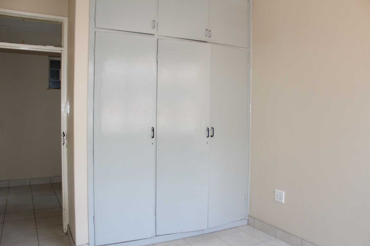 A simple bedroom featuring built-in cupboards with overhead storage and tiled flooring, offering a blank canvas for personalization.