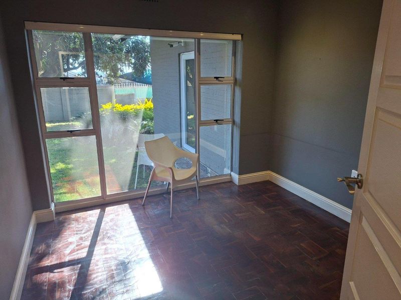A bright, empty living room featuring dark parquet flooring and large windows providing natural light and views of the rear garden.