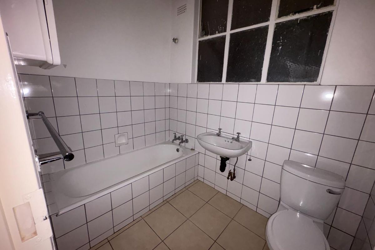 A dated bathroom featuring a standard bathtub, wall-mounted basin, and toilet with white wall tiles and neutral floor tiling.