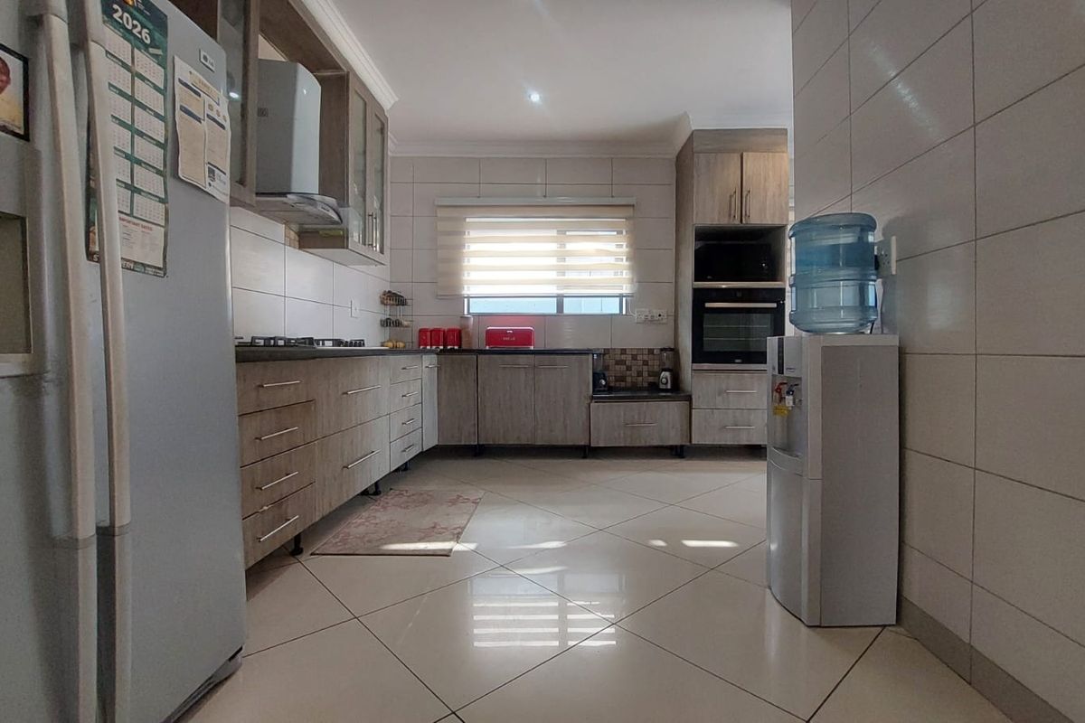 Modern kitchen featuring light wood-finish cabinetry, built-in oven, gas hob, extractor fan, and neutral tiled flooring with a clean, functional layout.