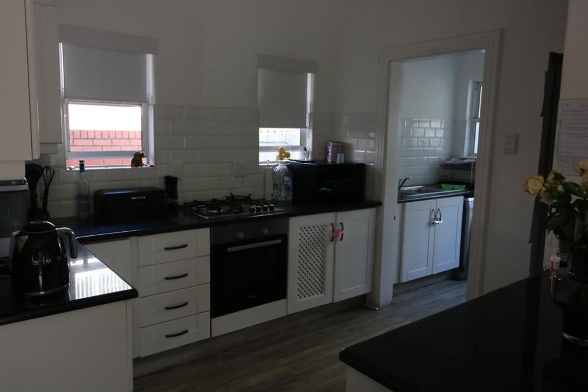 A functional kitchen featuring white cabinetry, subway tile backsplash, gas hob, built-in oven, and dark countertops, with an adjacent scullery area visible.