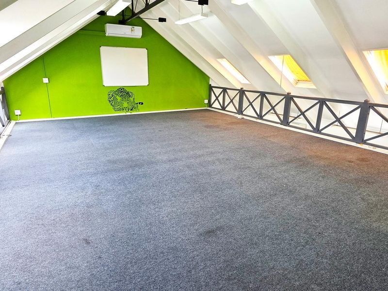 Spacious attic-style office area featuring carpeted flooring, multiple skylights for natural light, and a wall-mounted air conditioning unit.