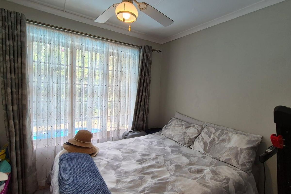 A bedroom featuring a ceiling fan and large window with views of the pool area.