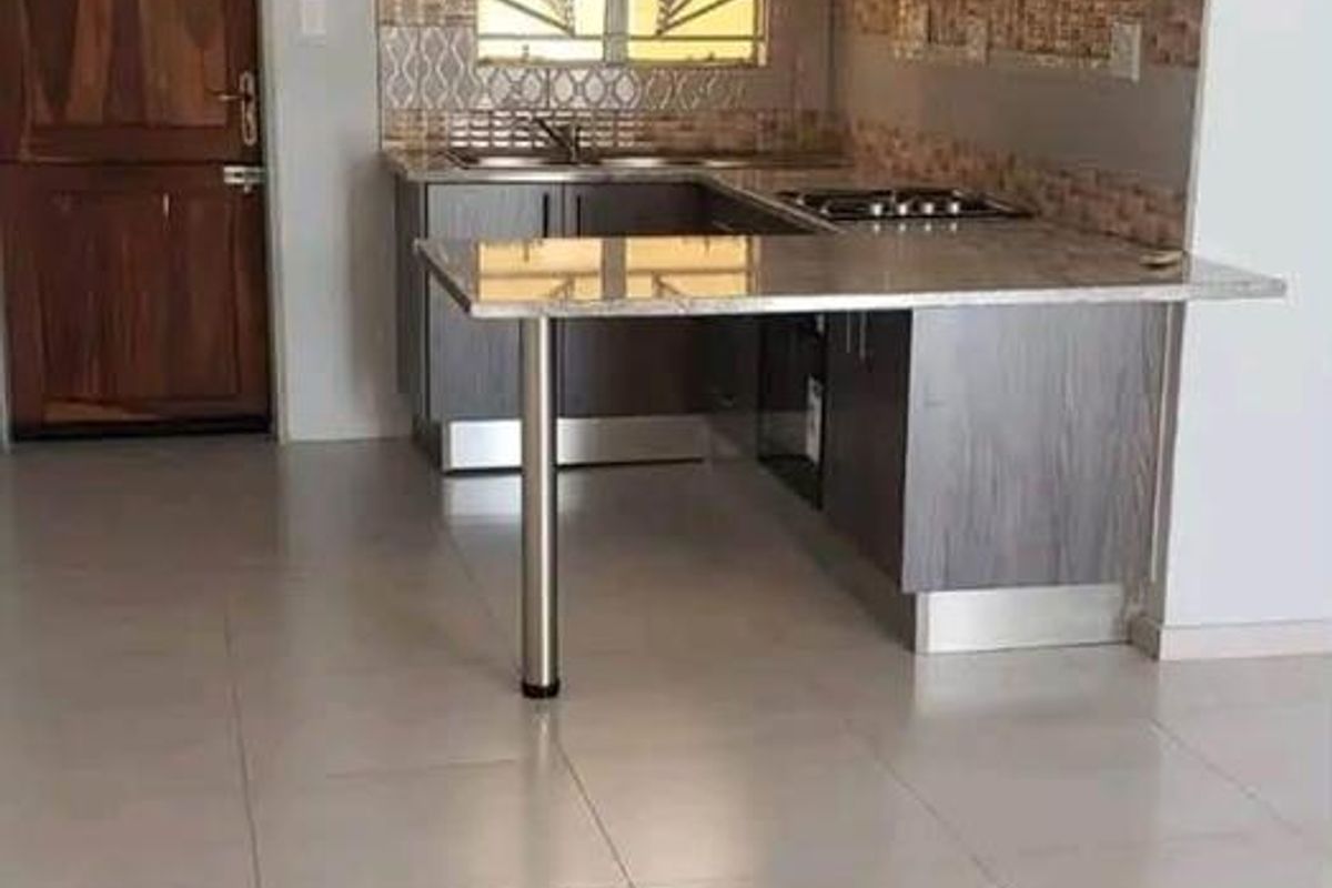 Modern kitchen featuring grey cabinetry, granite countertops with a breakfast bar, tiled backsplash, and integrated hob, set within an open-plan living space.