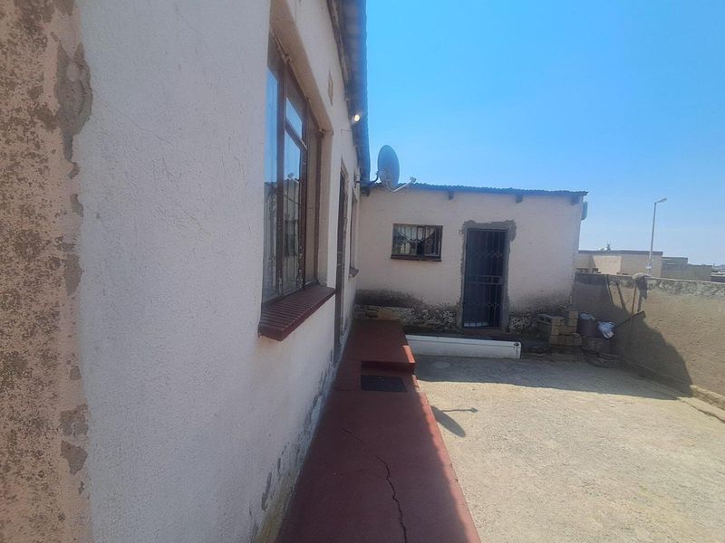 Rear exterior view of the property showing a concrete patio area, weathered wall finishes, and security features on windows and doors.