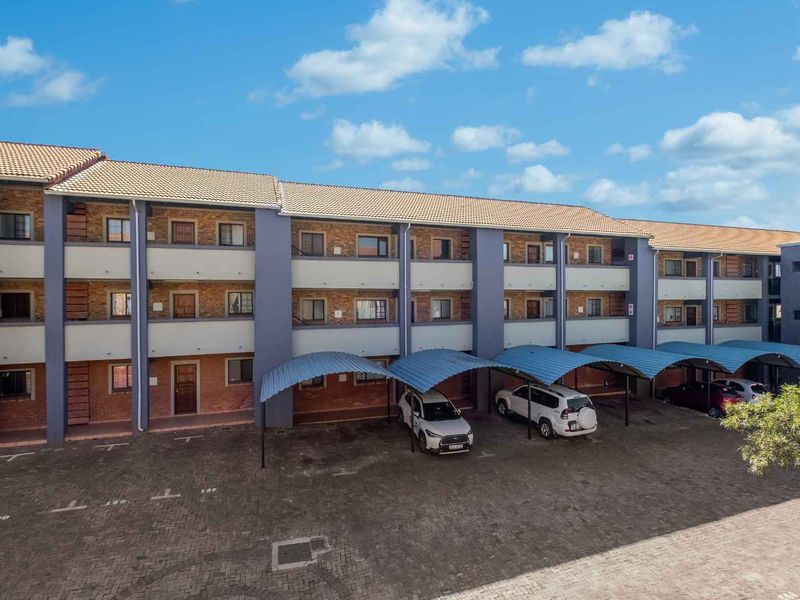 Exterior view of a multi-story apartment complex featuring brick and painted facade, tiled roofing, and dedicated covered parking bays.