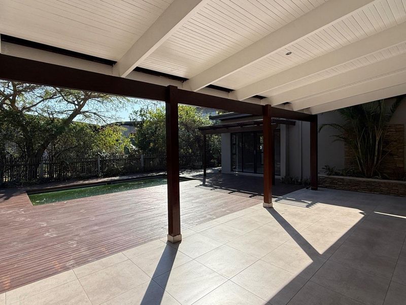 Spacious covered patio featuring timber decking and tiled flooring, overlooking a swimming pool and garden area, ideal for outdoor entertaining.