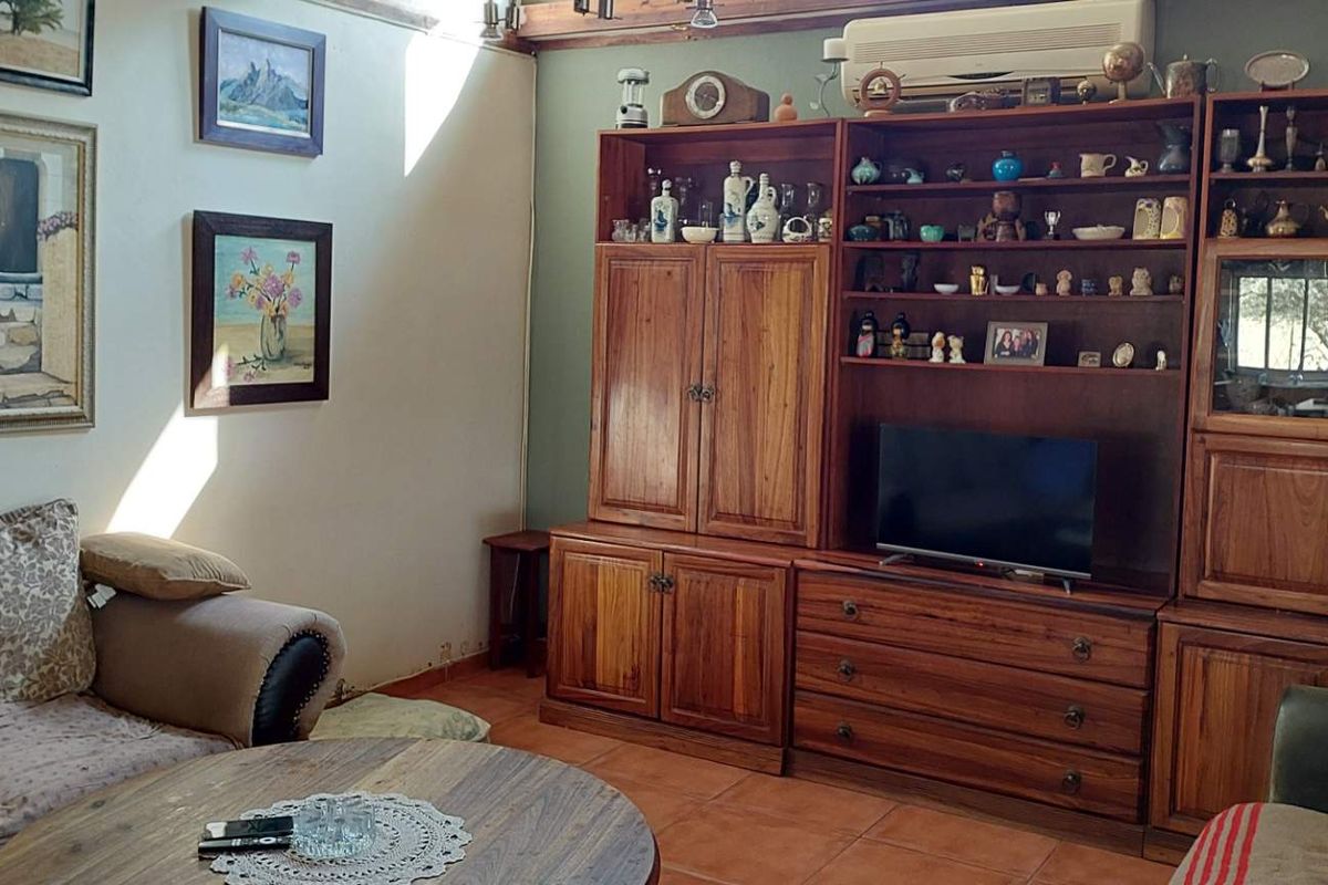 A living room featuring terracotta floor tiles, exposed wooden ceiling beams, and a wall-mounted air conditioning unit.