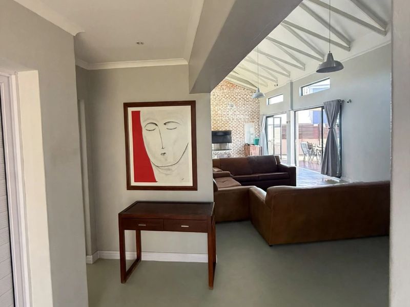 Spacious open-plan living area featuring exposed rafters, an exposed brick feature wall, and large sliding glass doors leading to an outdoor space.