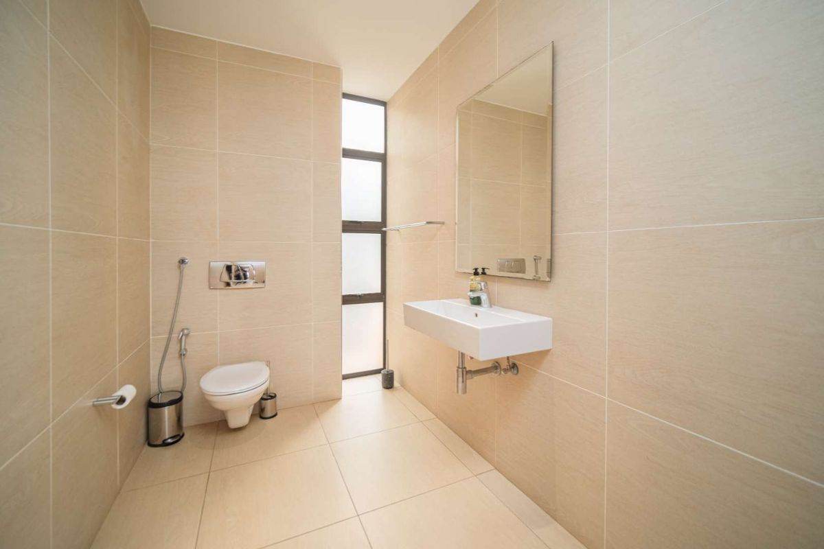 Modern bathroom featuring floor-to-ceiling neutral tiling, a wall-mounted basin, a concealed cistern toilet, and a tall vertical window for natural light.
