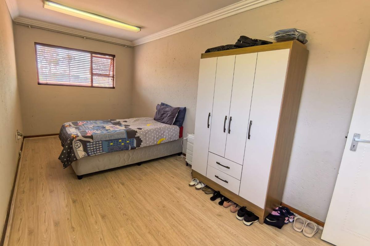 A bedroom featuring light wood-look laminate flooring, a window with blinds, and a built-in wardrobe.