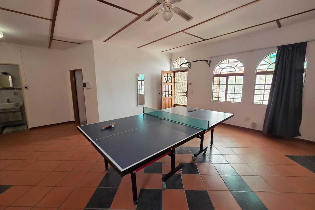 Spacious living area featuring tiled flooring, exposed ceiling beams, a ceiling fan, and arched windows providing natural light.